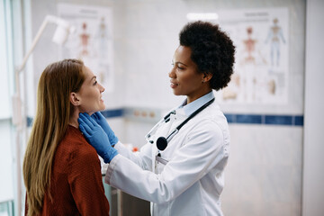 Smiling woman having thyroid exam by black female endocrinologist at medical clinic.