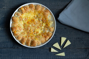 Cheese pie on a round white plate. Pieces of cheese, gray napkin. On a gray background.