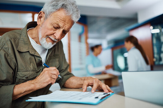 Mature man filling out medical paperwork at doctor's office.