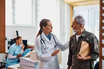 Fototapeta premium Female doctor communicating with senior man in hallway at medical clinic.