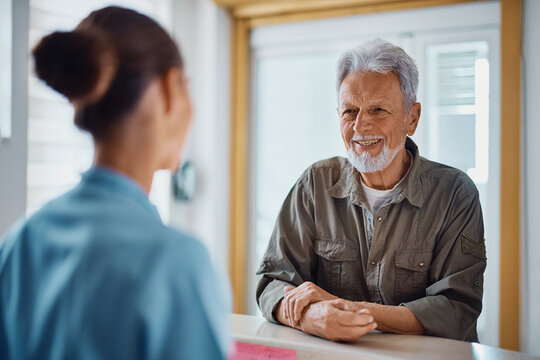 Happy senior man talks to nurse at reception desk at medical clinic.