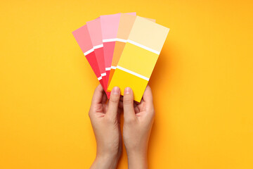 Female hand holding color palettes on yellow background