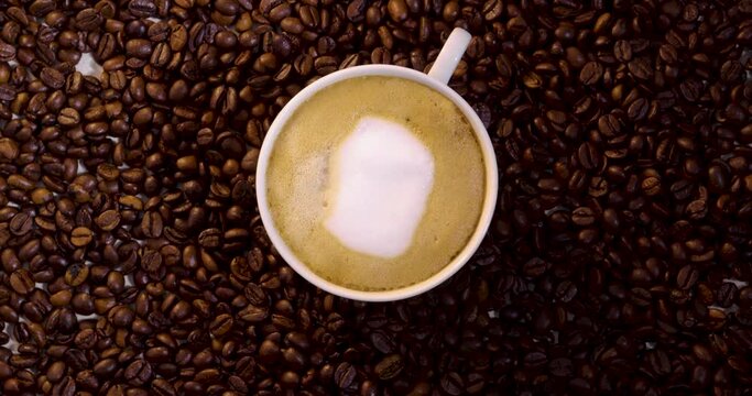 Birdseye View Of A Spinning Cup Filled With Foamy Coffee Latte And Cream Surrounded By A Pile Of Coffee Beans