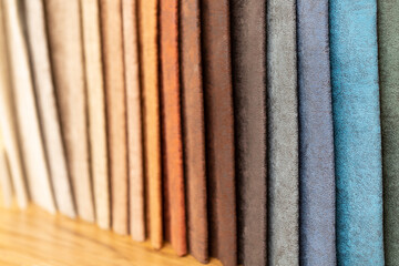 Fabric swatches in different colors are stacked for selection. A variety of shades of upholstery material for furniture and interior. Fabric texture close up. A set of multi-colored rolls of material.