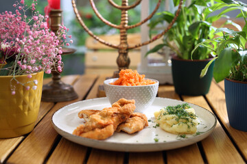 Lunch set - breaded chicken pieces, strips, potatoes and a carrot salad on a plate, on a wooden table, selective focus.