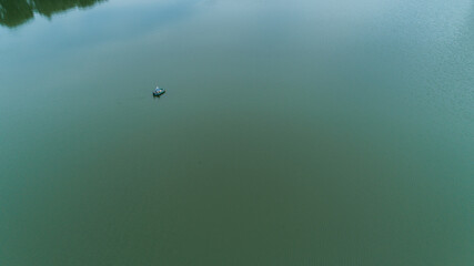 Aerial view fisherman is fishing sitting on an inflatable boat in lake. Drone wide shot adult man sailing on a boat to fish