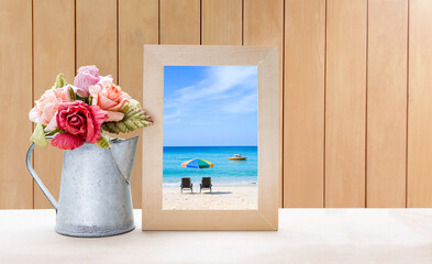 Beach picture in wooden frame with flower vase over wood background