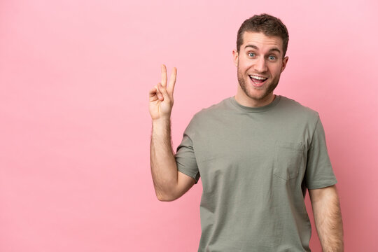 Young caucasian man isolated on pink background smiling and showing victory sign