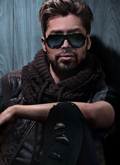 Obraz premium relaxed fashion man in sunglasses sits on wood in studio