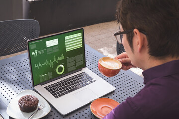 Over schouder zicht op Aziatische zakenman die koffie drinkt, met grafieken en diagrammen op laptopscherm