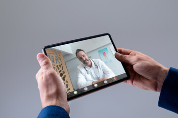 Hands of caucasian man making tablet video call with caucasian male doctor