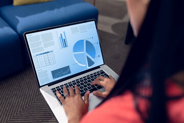Over shoulder view of biracial woman using laptop with data processing on blue interface screen