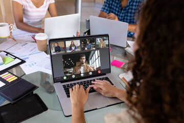 Biracial businesswoman in office making laptop video call with five diverse colleagues