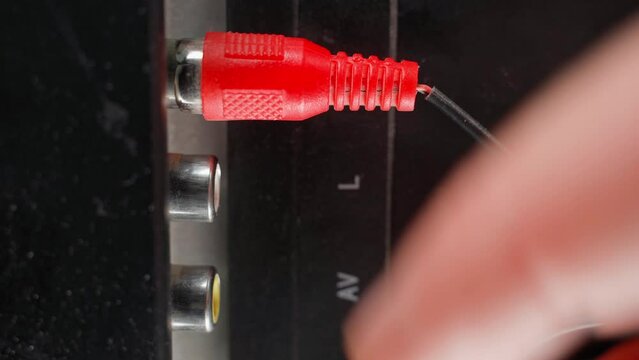 Hand inserts rca connectors of red white and yellow color from tv. Plug tulip of the old generation close-up. Wires for transmitting audio and video signals are thin, poor quality
