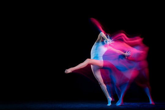 Ease of movement. Tender female ballet dancer dancing solo dance over dark background in mixed neon light. Art, flexibility, inspiration and beauty concept.