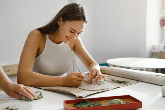 Pottery workshop in studio. Young woman working with clay on the table. Adult female learning to do ceramic plates. Pottery as hobby and leisure activity
