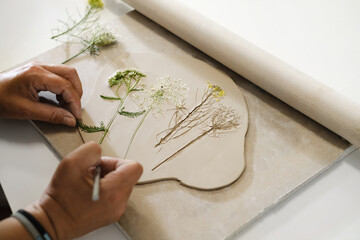 Hands making Clay handmade Ceramic plates, rolled clay on the table with plants and flowers. Top...