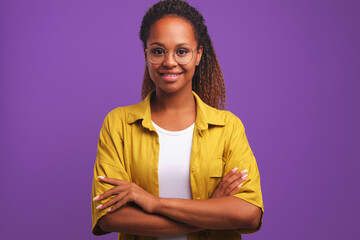 Obraz na płótnie Canvas Young successful positive African American woman student arms crossed in front of chest looks at camera demonstrating purposefulness and self-confidence stands on studio plain background