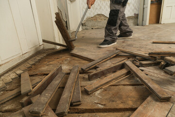 Home improvement. Construction worker or handyman is removing old wooden parquet flooring using crowbar tool. Old wooden floor renovation.	