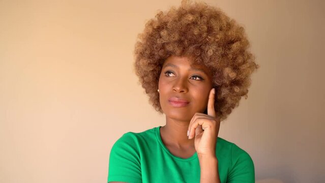 Attractive dark-skinned woman looking at camera and smile. Thinking creative ideas. happy search solution. thoughtfully touching face with hand looks up, laughing. Video footage. beige background