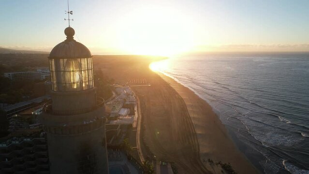 aerial shot over the maspalomas lighthouse, approaching and exceeding the lighthouse. Shot taken at golden hour and with the lighthouse on. wonderful colors