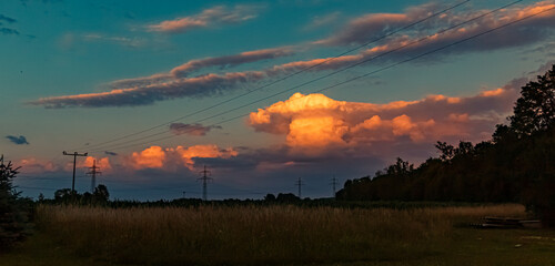 Beautiful sunset with a dramatic sky and overland high voltage lines near Tabertshausen, Bavaria, Germany