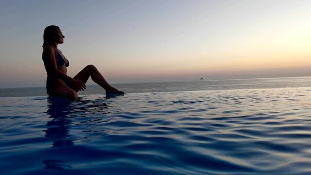 Beautiful woman relax in infinity swimming pool at luxury hotel spa enjoy golden sunset view of ocean mediterranean travel holiday resort. Female silhouette High quality slow motion 4k raw video