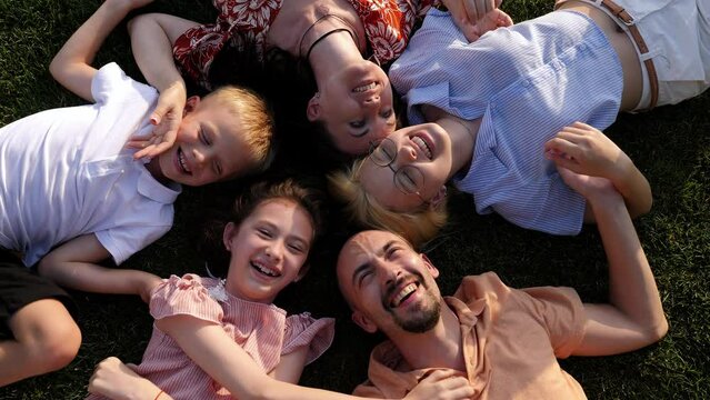 A big happy family lies on a green lawn in a circle and laughs. Top view.