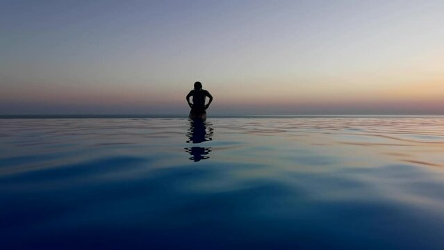Beautiful woman relax in infinity swimming pool at luxury hotel spa enjoy golden sunset view of ocean mediterranean travel holiday resort. Female silhouette High quality slow motion 4k raw video