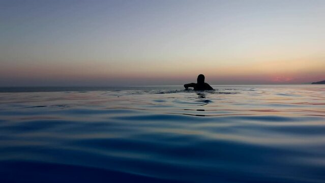 Beautiful woman relax in infinity swimming pool at luxury hotel spa enjoy golden sunset view of ocean mediterranean travel holiday resort. Female silhouette High quality slow motion 4k raw video