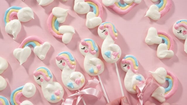 Flat lay. Gourmet unicorn theme meringue pops on a pink background.