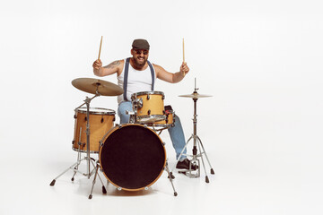 Portrait of emotive, expressive man in sunglasses playing drums, performing isolated over white...