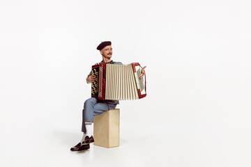 Portrait of young emotive man playing accordion, posing isolated over white studio background