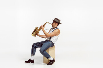 Portrait of stylish man in hat and suglasses playing saxophone , performing isolated over white background. Puffy cheeks