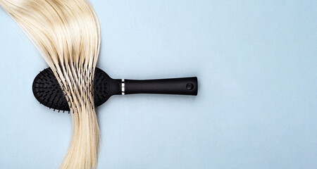 Closeup of Black hair brush lying on straight shiny blond hair. Hair care and styling concept. Abstract background for hairdresser business.