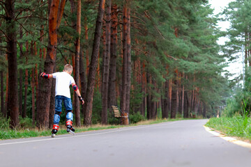 A boy on roller skates in the park, on an asphalt road. Rear view