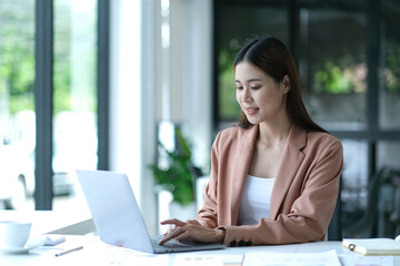 Charming asian businesswoman sitting working on laptop in office.