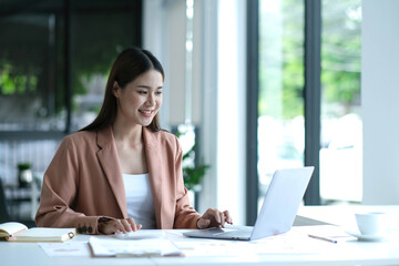 Fototapeta premium Beautiful Asian businesswoman analyzes charts using laptop calculator at the office.