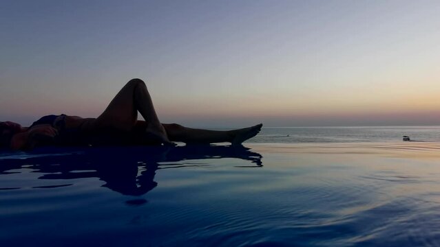 Beautiful woman relax in infinity swimming pool at luxury hotel spa enjoy golden sunset view of ocean mediterranean travel holiday resort. Female silhouette High quality slow motion 4k raw video