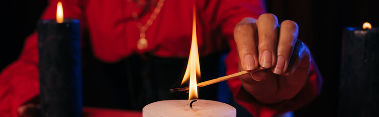 partial view of fortune teller lighting palo santo stick near burning candle isolated on black, banner.