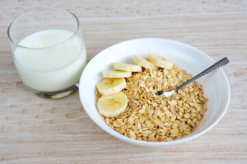 oatmeal flakes with banana slices in white bowl and teaspoon, close-up