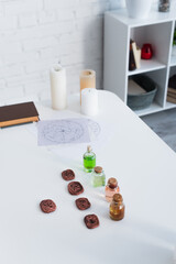 clay runes and bottles with essential oils near star charts and candles on white table.