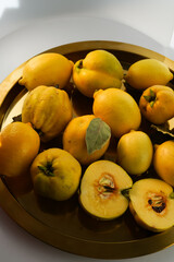 a lot of ripe quince with leaves and one cut in a large gold platter on a white plate with bright daylight 