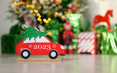 The inscription 2023 on a toy New Year's car against the background of a Christmas tree and gifts. The concept of the new 2023. copyspace.