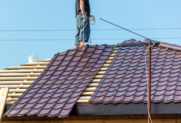 Fototapeta premium Workers install metal roofing on the wooden roof of a house.
