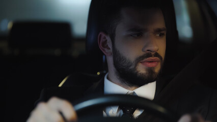 young businessman looking aside while driving car at night.
