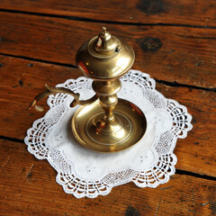 Palmatoria antigua de bronce sobre un paño blanco bordado y una mesa de madera antigua. Detalle de...