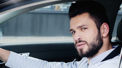 young and confident man driving car and looking at camera.