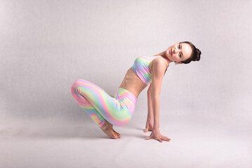 A beautiful slender gymnast in a stretch in a tracksuit does sports or yoga in the studio flexibly...