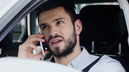 young man talking on cellphone and looking away while driving automobile.